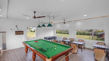 A pool table with surrounding chairs and tables, a ceiling fan, and a view of the outdoors.
