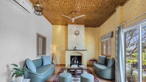 A living room with a fireplace, two sofas, a coffee table, and a ceiling fan. - Krishna Serenity Petfriendly 7BHK Farm (Peesangan)