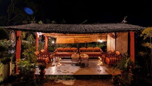 A thatched-roof outdoor seating area with wooden furniture and potted plants. - Krishna Serenity Petfriendly 7BHK Farm (Peesangan)