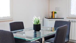 Een moderne vergaderruimte met een glazen tafel, vier grijze stoelen, een zwarte vaas met groene planten en een whiteboard aan de muur.