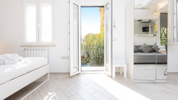 Een moderne slaapkamer met een bed, een klein nachtkastje, een spiegel en een balkondeur.
