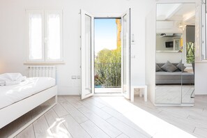 A modern bedroom with a bed, a small bedside table, a mirror, and a balcony door. - Monti Terrace (Rome)