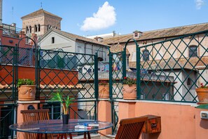 A glass table with chairs, a potted plant, and a view of a historic building with a bell tower. - Monti Terrace (Rome)