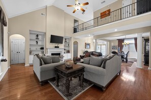 A spacious living room with a fireplace, a television, and a dining area with a chandelier. - Spacious Lakefront Home | Memphis Retreat (Memphis)