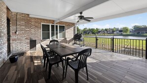 Eine überdachte Terrasse mit Tisch, Stühlen, einem Grill und Blick auf einen See und Häuser.