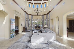 A spacious lobby with a large sectional sofa, a chandelier, and a view of the outdoors through large windows. - Poolside Resort Condo- CLOSEST To Theme Parks!! (Orlando)