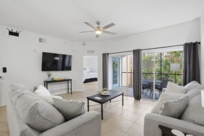 A modern living room with two sofas, a coffee table, a flat-screen TV, and a ceiling fan. - Poolside Resort Condo- CLOSEST To Theme Parks!! (Orlando)