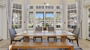 Un espace repas comprenant une grande table, des chaises et une vue dégagée grâce à de larges fenêtres.