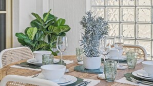 A dining table set with white plates, bowls, and clear glassware, surrounded by wicker chairs. - Riviera 102: 2  BR, 2  BA Apartment in Port Macquarie, Sleeps 4 (Port Macquarie)