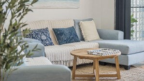 A living room with a grey sofa, a round wooden coffee table, and a large window with a view of the ocean. - Riviera 102: 2  BR, 2  BA Apartment in Port Macquarie, Sleeps 4 (Port Macquarie)