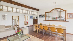 A modern living room with a sofa, coffee table, and dining area with chairs and a wooden table. - Family cottage for 6, share pool & garden (Fanlac)