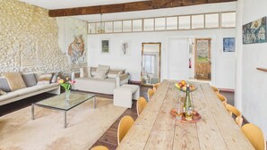A spacious living area with a long wooden dining table, a sofa, and a stone wall. - Family cottage for 6, share pool & garden (Fanlac)