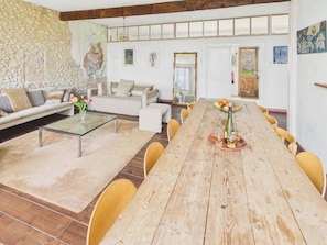 Un vaste espace de vie comprenant une longue table à manger en bois, un canapé et un mur en pierre.