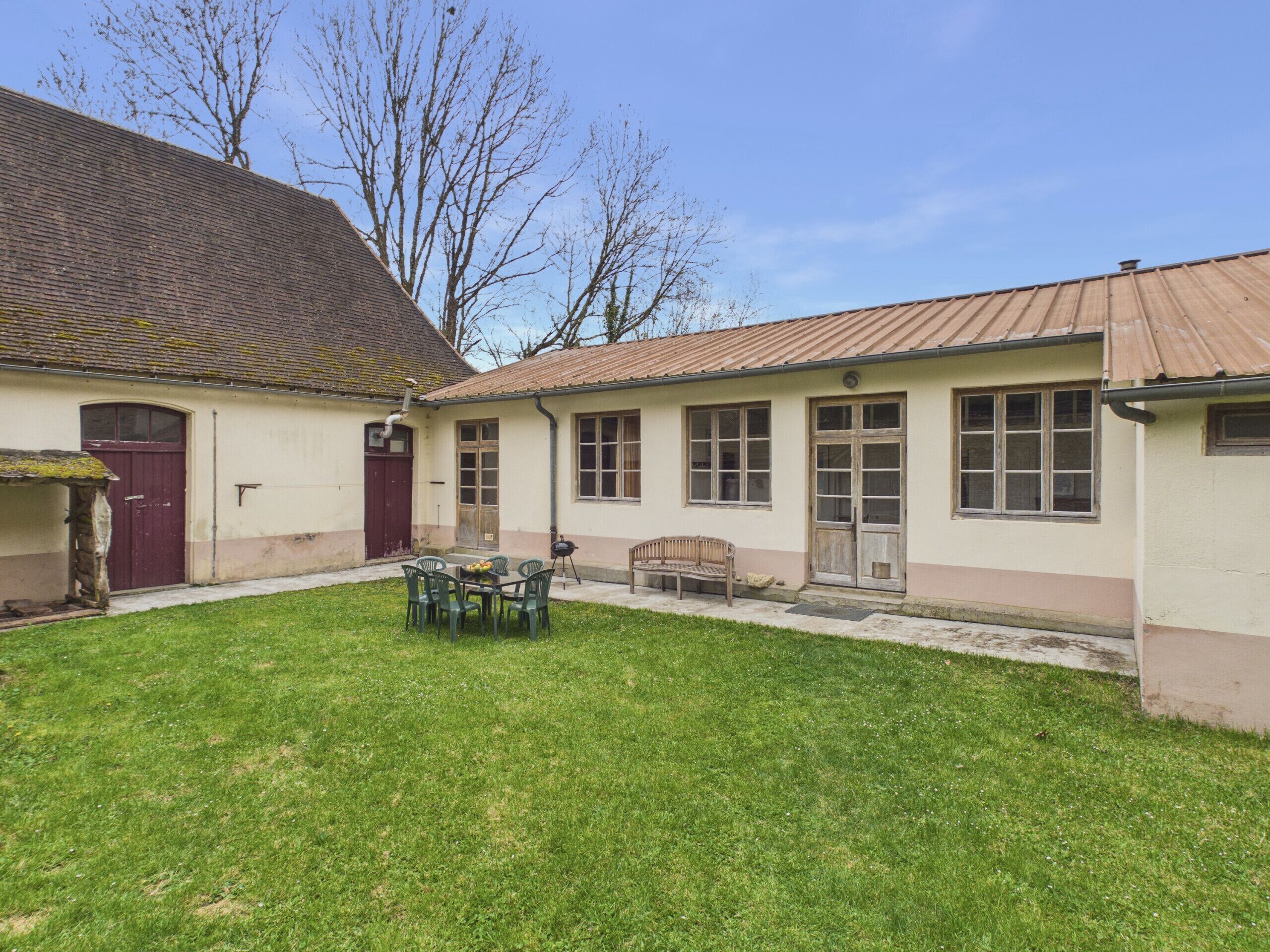 A building with a tiled roof, a grassy courtyard, and a bench.