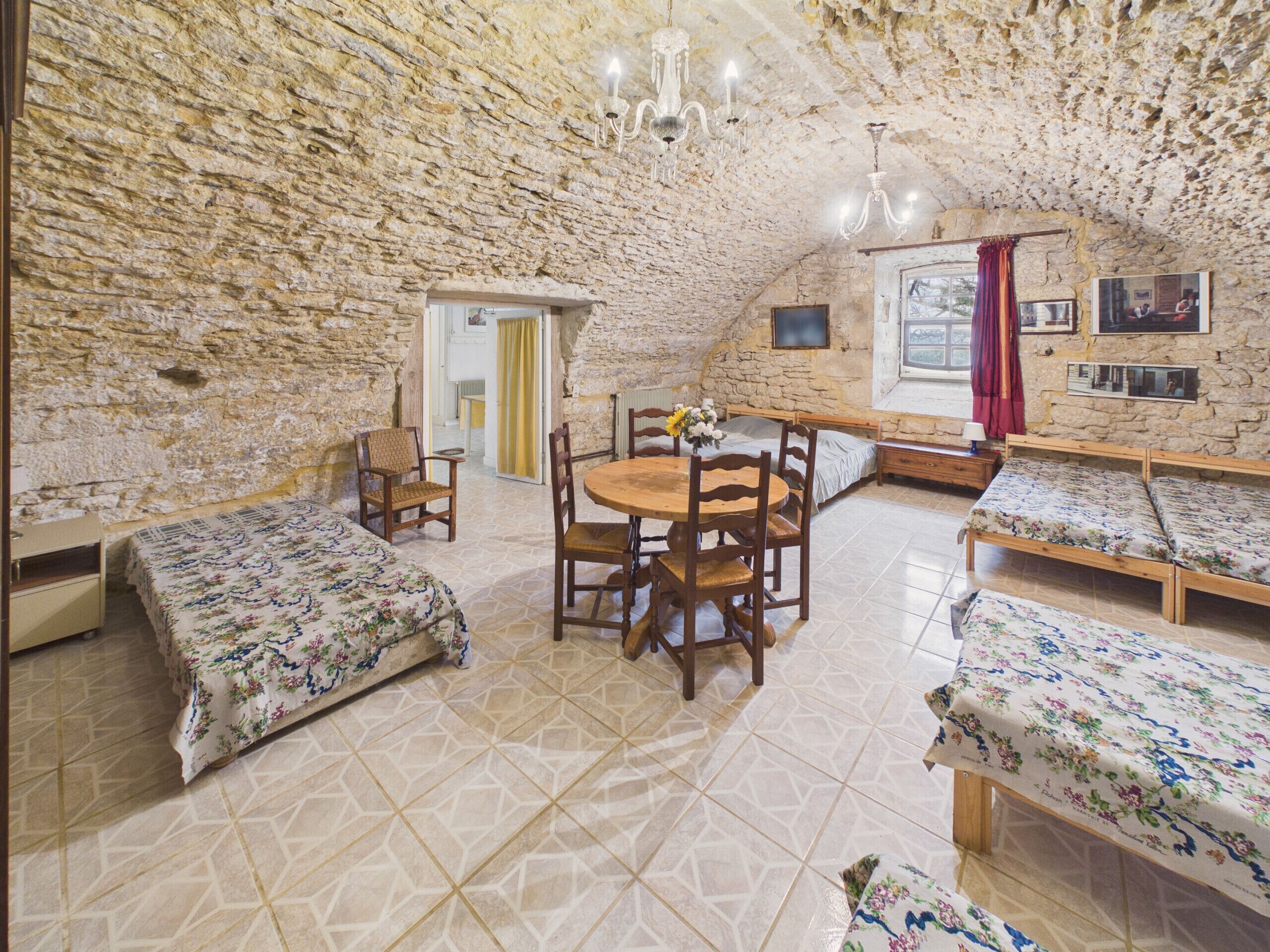 Una habitación rústica con paredes de piedra, una mesa redonda de madera, dos camas de madera y un televisor pequeño en la pared.
