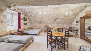 Ein rustikaler Raum mit Steindecke, einem Holztisch und mehreren Betten.