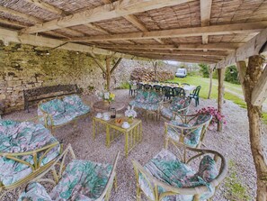 Une terrasse extérieure aménagée avec des meubles en osier, un mur en pierre et une table dressée pour le repas.