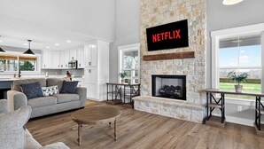Ein modernes Wohnzimmer mit Kamin, einer Wand-Fernseher und Blick ins Freie.