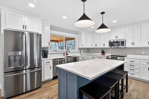 A modern kitchen with stainless steel appliances, white cabinetry, and a marble island.