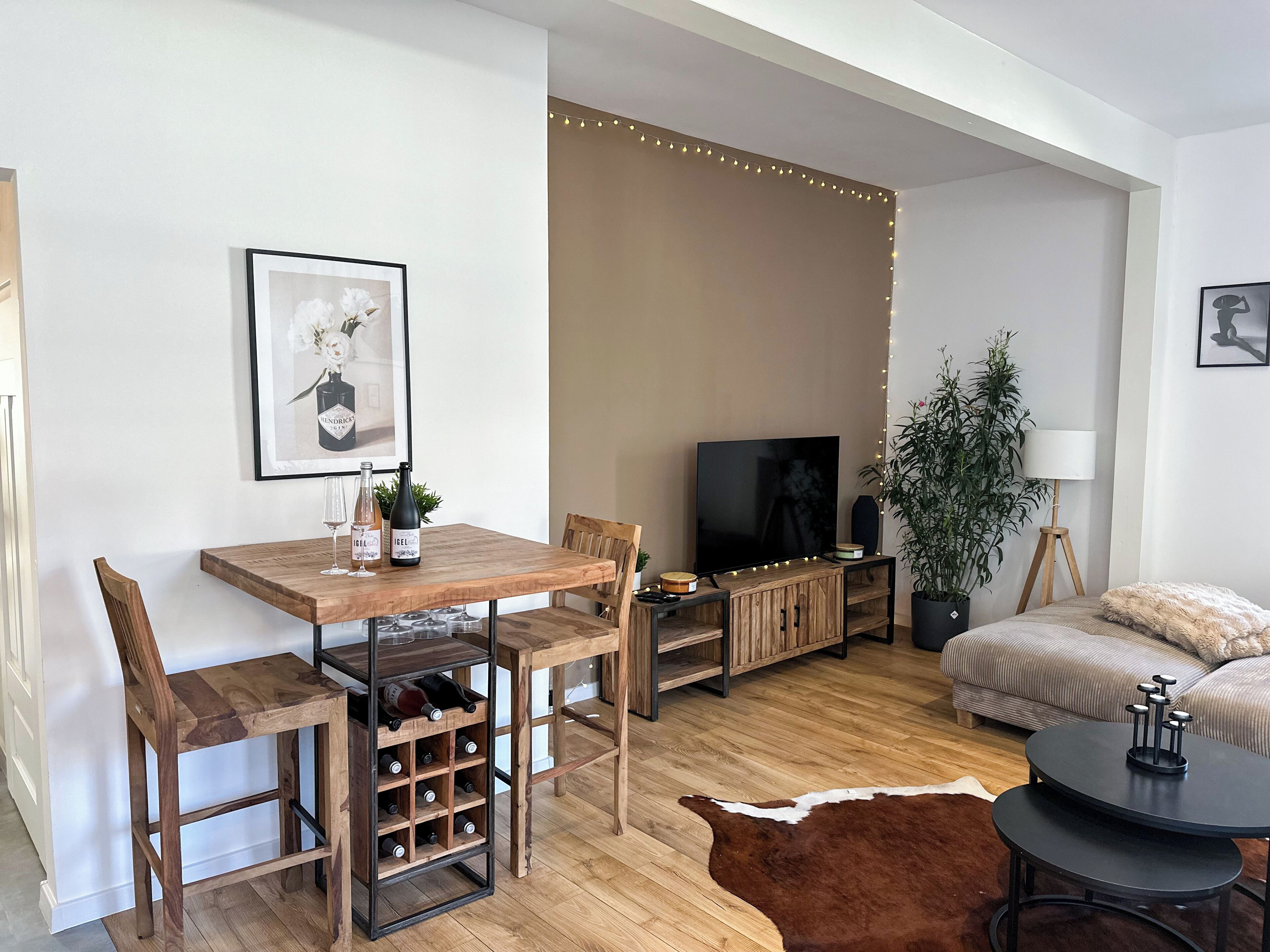 Un salon moderne avec une table à manger en bois, des chaises, un téléviseur, un canapé, une petite table ronde et un tapis en peau de vache.