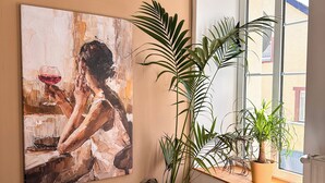 Una stanza con un quadro astratto di grandi dimensioni, una pianta in vaso, una finestra vista e un pavimento in legno.