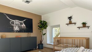 Camera da letto moderna con un letto grande, una culla, un mobile consolle grigio, una TV a muro e una pianta in vaso.