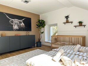 A modern bedroom with a large bed, a crib, a grey console, a wall-mounted TV, and a potted plant. - Tasteful vacation home for the whole family (Densborn)