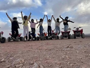 A group of people standing on a rocky terrain with their arms raised, surrounded by ATVs.