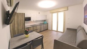 Un espacio habitable compacto con kitchenette, un comedor con mesa y sillas, y un sofá.