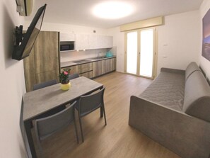 A compact living space with a kitchenette, a dining area with a table and chairs, and a sofa. - Modern Flat With Garden and Gazebo (Lignano Sabbiadoro)