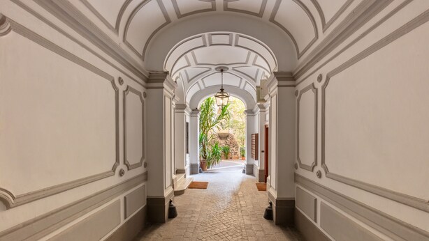 A corridor with a tiled floor, white walls with decorative moldings, and an arched ceiling. - DEZA| Monti Incanto Boutique Apartment (Roma)