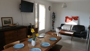 A dining area with a wooden table set for four, a vase with flowers, and a television mounted on the wall. - GÏTE DE LA CHAPELLE (Talissieu)