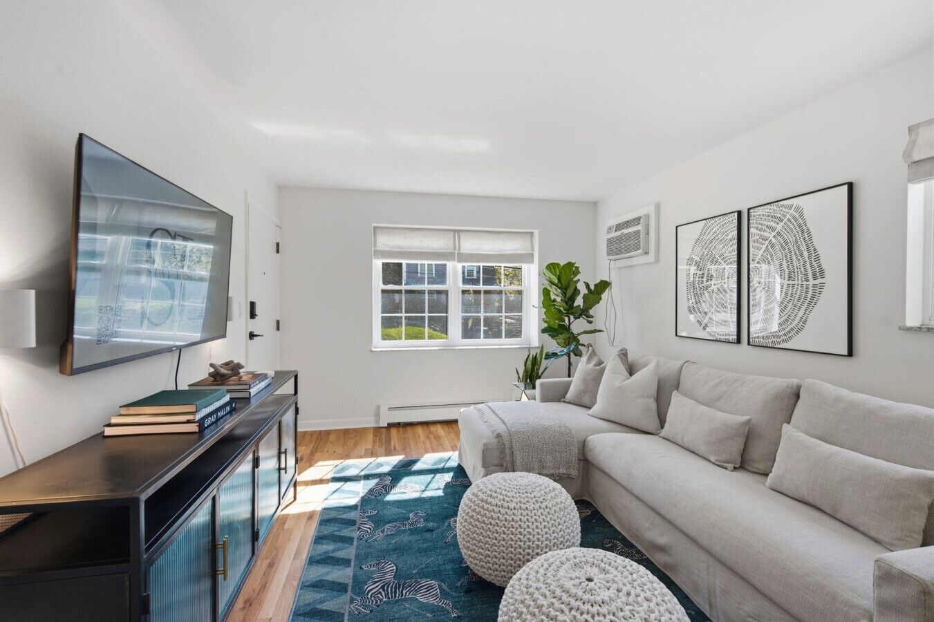 A living room with a flat-screen TV, a sofa, a coffee table, a bookshelf, a window, and artwork on the wall.