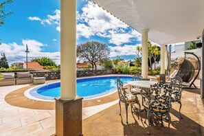 Un área de piscina con una pileta circular, mobiliario exterior y un patio cubierto.