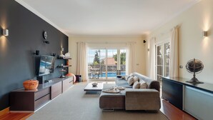 Un salon moderne avec un canapé, une table basse et un téléviseur, un balcon avec vue sur la piscine et un coin repas.
