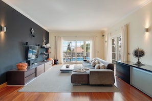 Una sala de estar moderna con sofá, mesa de centro y televisor, un balcón con vista a la piscina y un comedor.