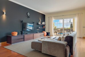 Una sala de estar moderna con un televisor de pantalla plana, muebles de madera oscura, un ventanal con vistas al exterior y un rincón de estar acogedor.