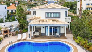 Une maison à deux étages avec une piscine, un patio doté de chaises longues et un espace extérieur aménagé et couvert.