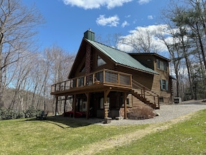 A log cabin with a balcony, a chimney, and a gravel driveway.