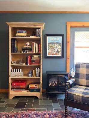 A living room with a bookshelf, a framed poster, a fireplace, and a plaid sofa.