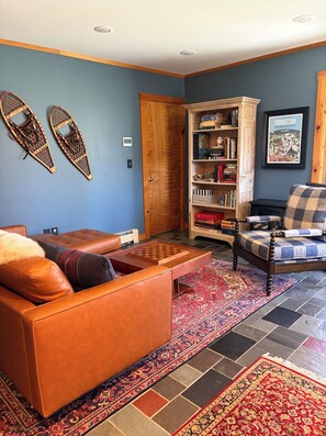 A living room with a brown leather sofa, a wooden coffee table, a bookshelf, and a patterned rug. - Cozy Waterfront Guesthouse Getaway in Camden with Mountain Views (Camden)