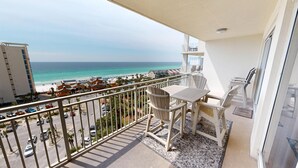 Een balkon met uitzicht op het strand, een tafel en stoelen.