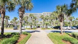 Een hotelingang met een verhard pad, palmbomen en geparkeerde auto's.
