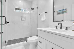 Ein modernes Badezimmer mit Duschkabine aus Glas, Toilette in Weiß, Waschbecken in Weiß mit großem Spiegel und Handtuchhalter.