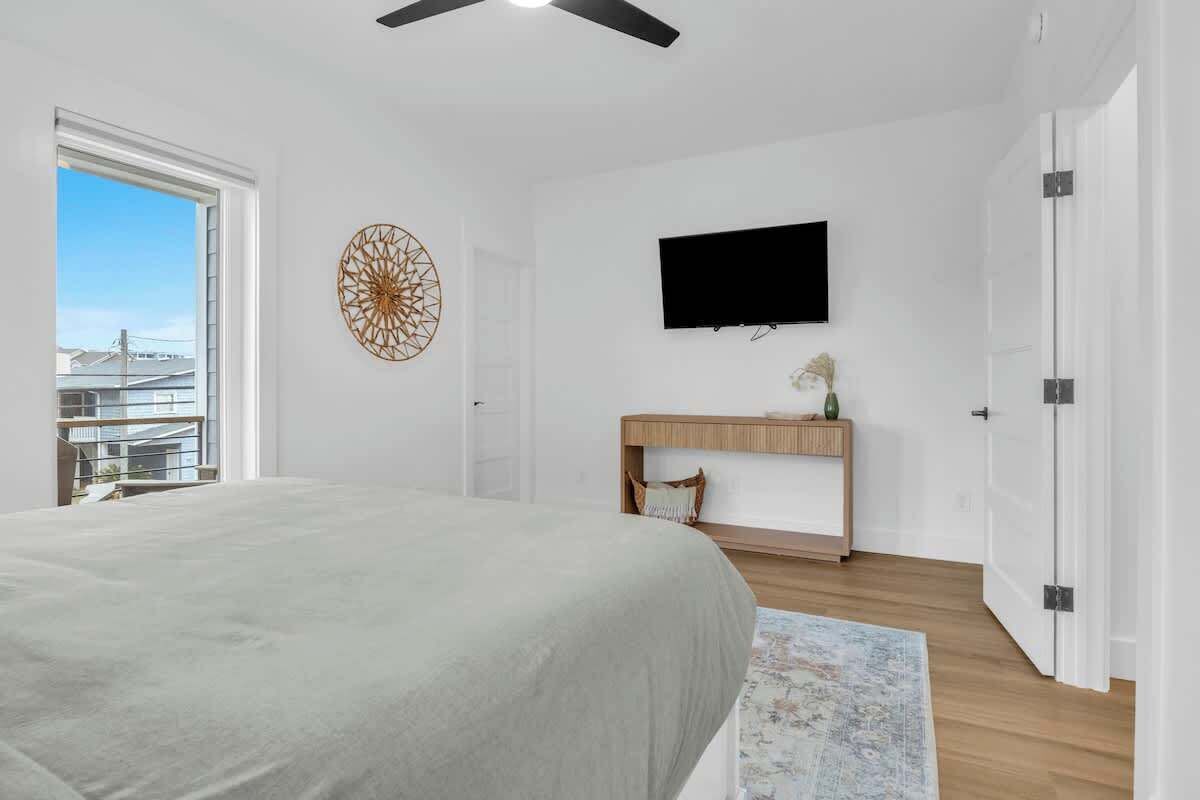 Une chambre à coucher avec un lit, un téléviseur fixé au mur, une console en bois et une vue sur l’extérieur par une porte ouverte.