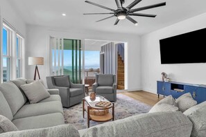 Ein modernes Wohnzimmer mit Sofa, Sesseln, Couchtisch, Fernseher und Deckenventilator.