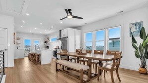 A modern kitchen with a dining area, wooden flooring, and a ceiling fan. - SeaView Rooftop-Steps To Beach w/Parking/Elevator! (Carolina Beach)