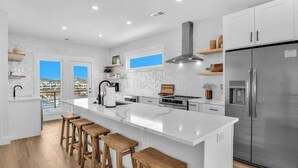 A modern kitchen with a large island, stainless steel appliances, and wooden stools. - SeaView Rooftop-Steps To Beach w/Parking/Elevator! (Carolina Beach)