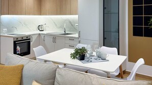 Een moderne keuken met een marmeren spatwand, houten keukenkastjes, een kast met glazen deurtjes en een eethoek met een witte tafel en stoelen.