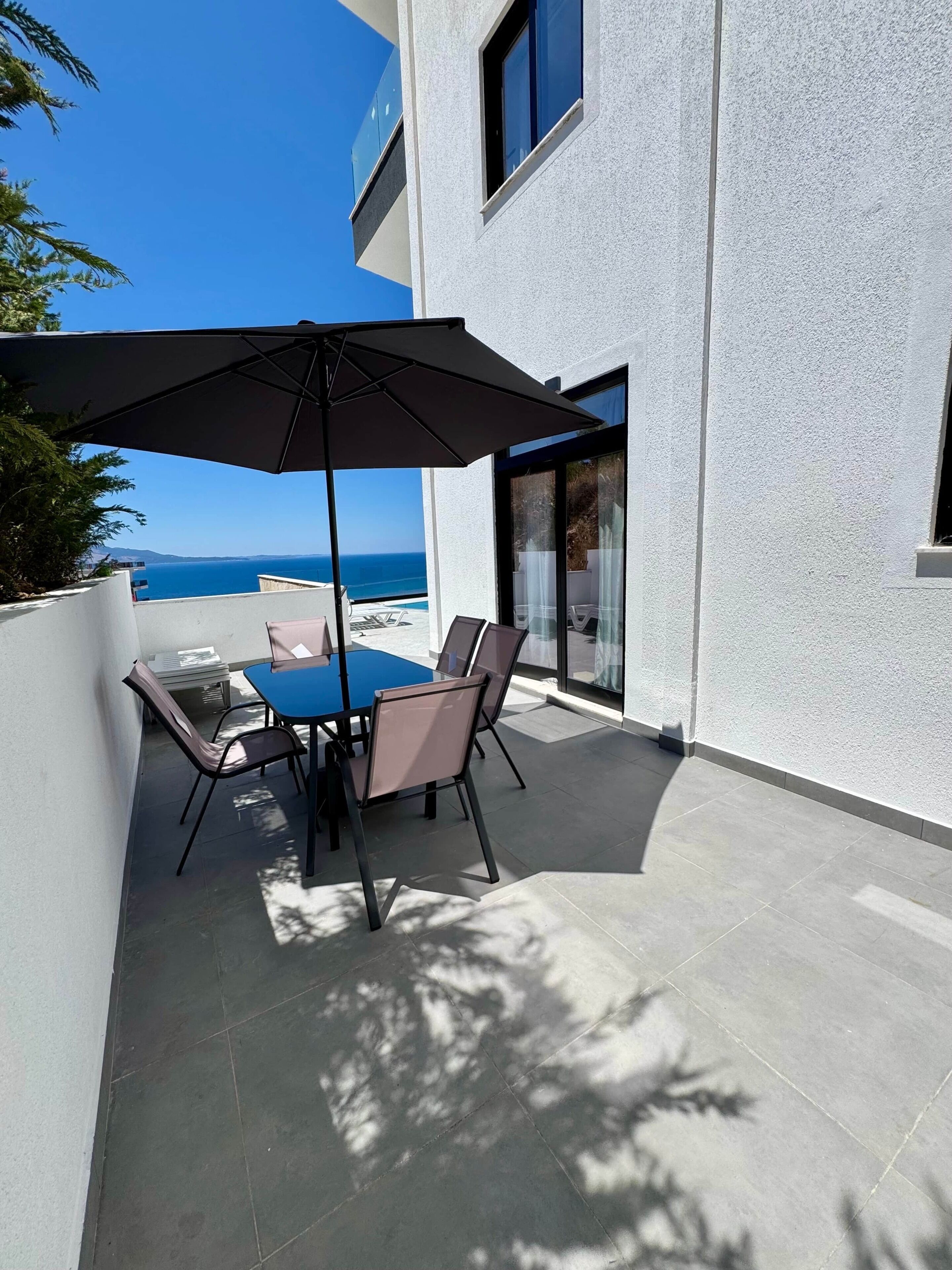 Une terrasse extérieure avec une table et des chaises, un grand parasol et une vue sur la mer.
